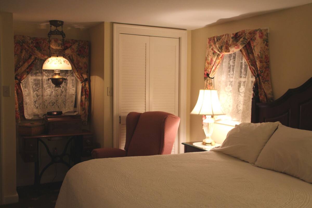 Une chambre d’hôtel avec un lit, une chaise, un bureau avec une lampe et des rideaux.