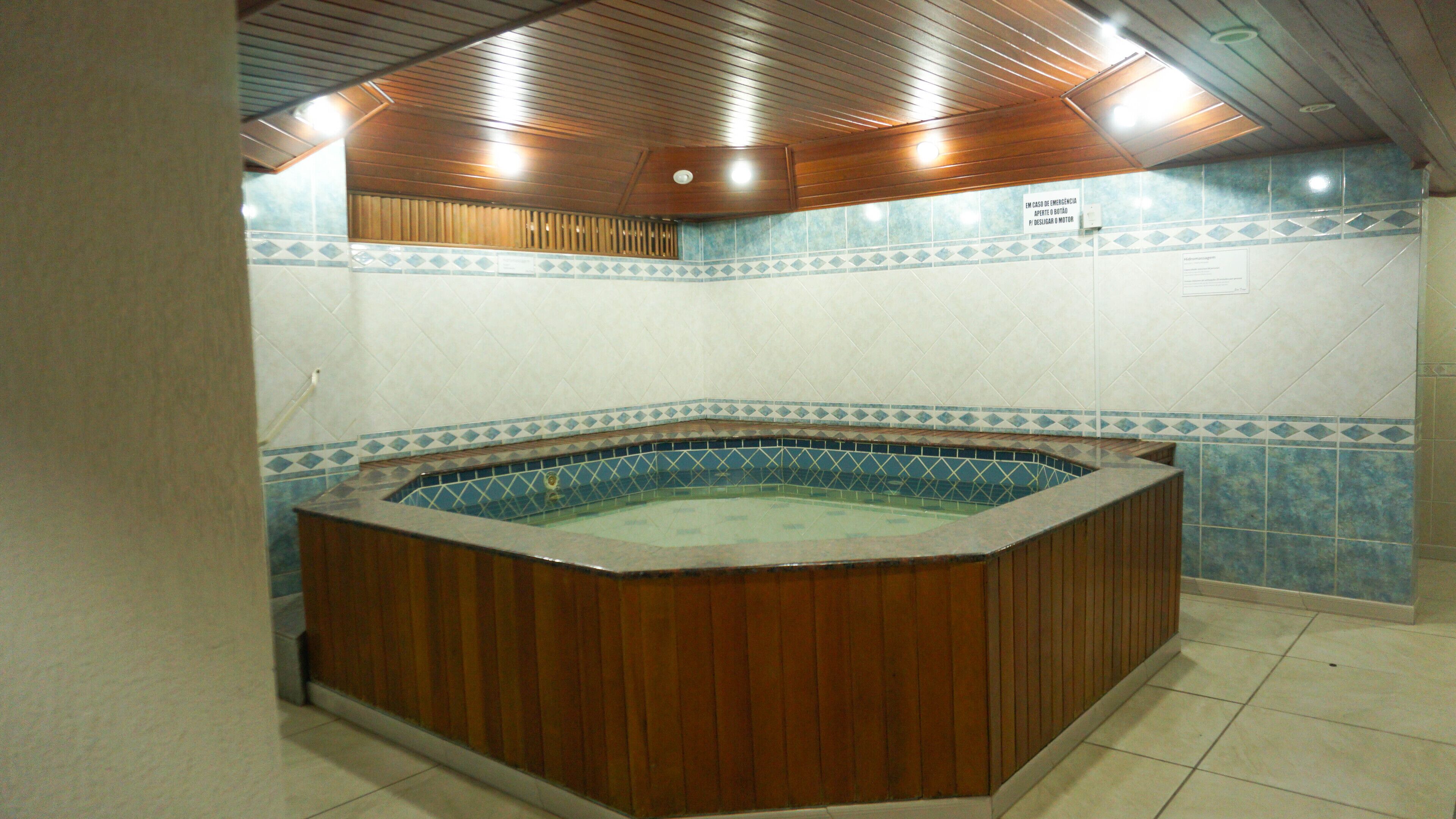 A hot tub with wooden walls and blue-tiled floor, surrounded by a tiled wall with a decorative border.