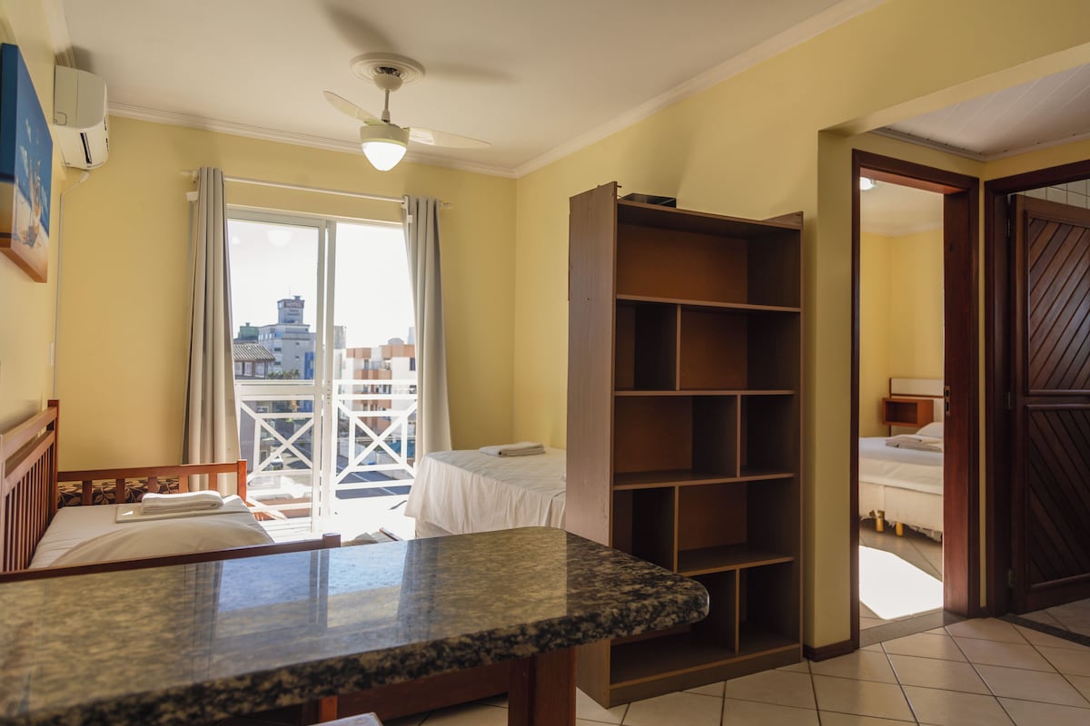 Habitación de hotel con cama, armario de madera, balcón con vistas a edificios y ventilador de techo.