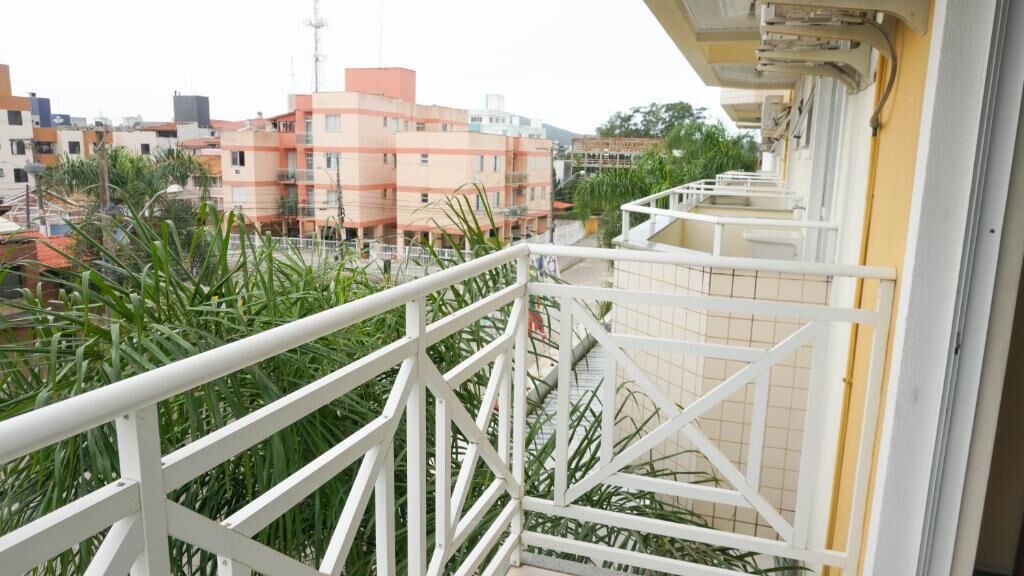 Varanda com guarda-corrimão branco, vista para uma área residencial com edifícios e vegetação.