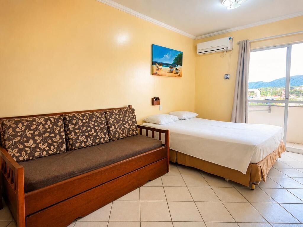 A room with a sofa and a bed, a painting on the wall, and an air conditioning unit.