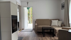 A modern living room with a sofa, a coffee table, and a TV. There is a door leading to an outdoor area with a view of trees. - Baltic Sea holiday home in a quiet location - only 200 m to the beach, dogs welcome, W-LAN  (Pobierowo)