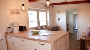 A kitchen with a wooden countertop, white cabinets, a coffee maker, a toaster, and a bowl. There is a window above the counter and a door leading to another room. - Haus Hanna (Dagebuell)