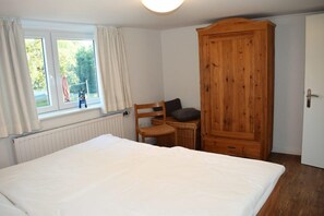 Un dormitorio con cama, armario de madera, silla y ventana con cortinas.