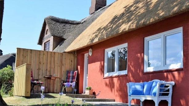 A red house with a thatched roof, a wooden fence, a bench, and a small table with chairs outside. - Haus Hanna (Dagebuell)