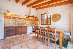 A kitchen with wooden cabinets, a tiled backsplash, a dining table with chairs, and a window with a view. - Country House with Romantic Patio and Pool – Finca Ca'n Vaqueta (Soller)