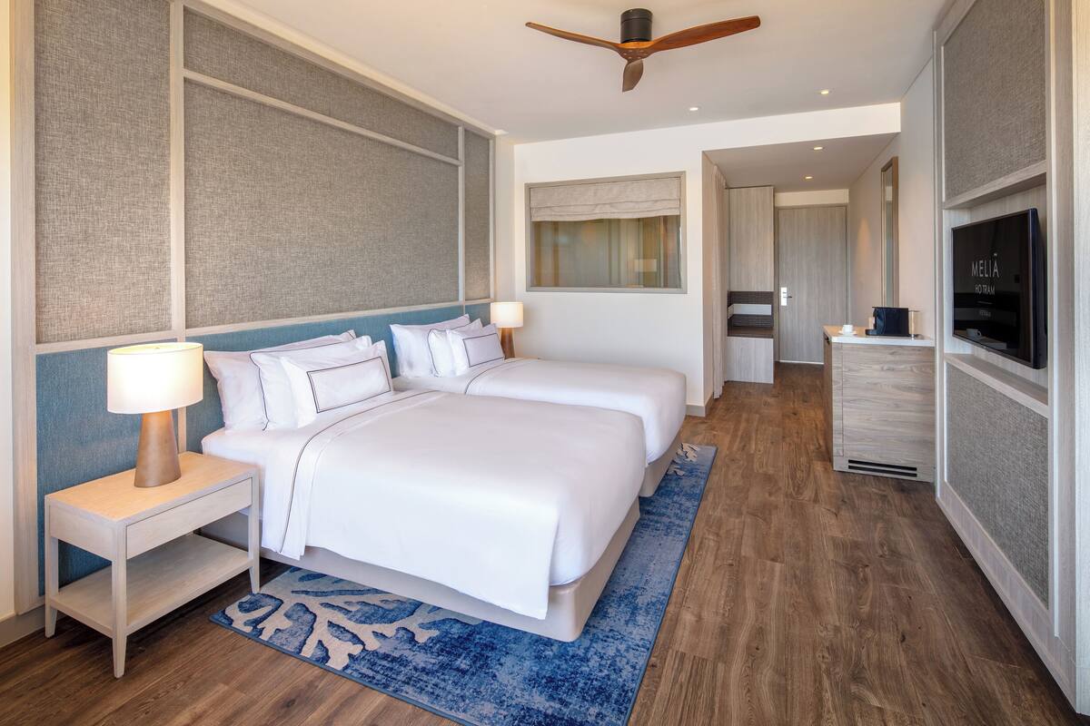 Een hotelkamer met een bed, nachtkastjes, een televisie en een plafondventilator.