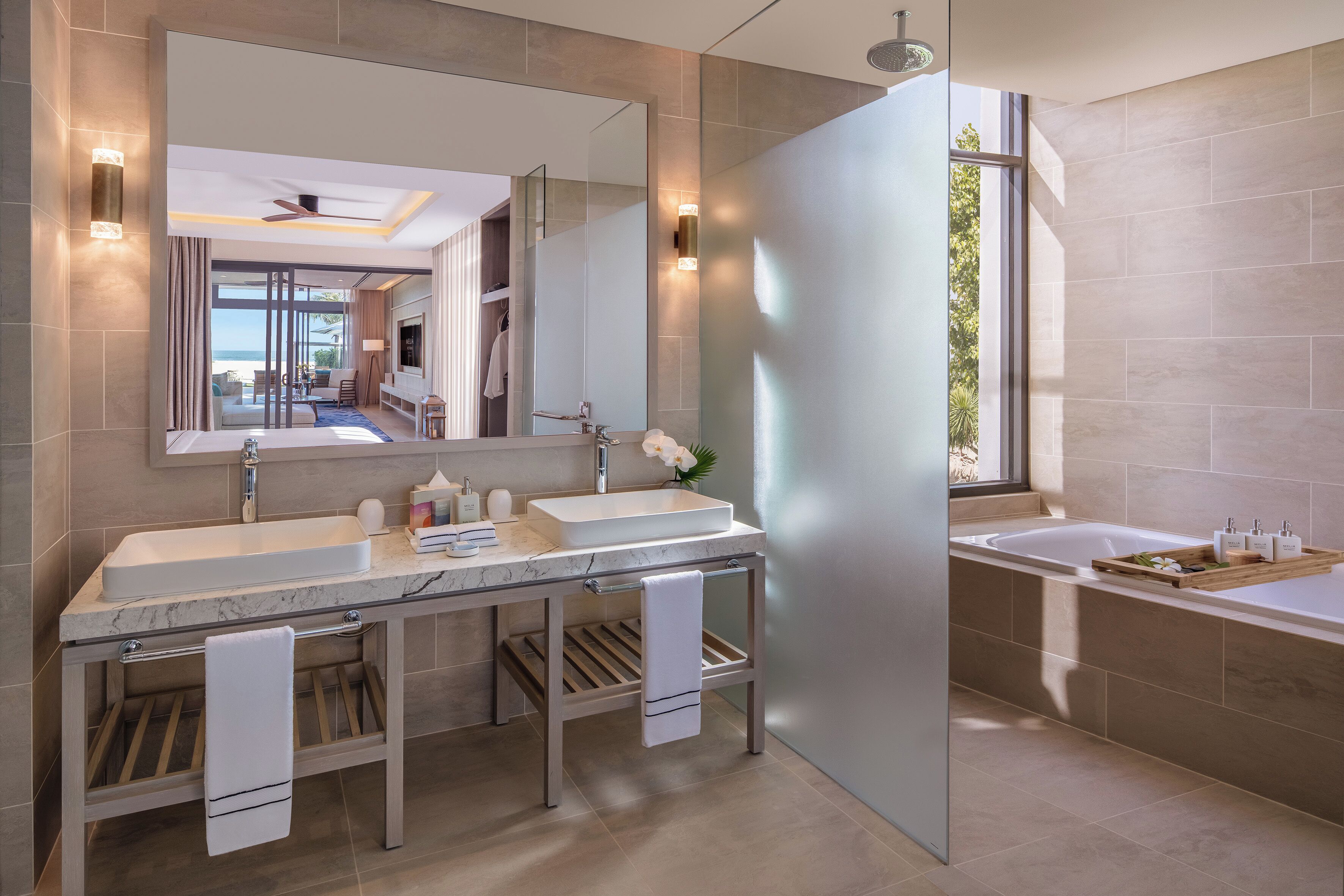 A modern bathroom with a large mirror, dual sinks, a bathtub, and a view of the outdoors.