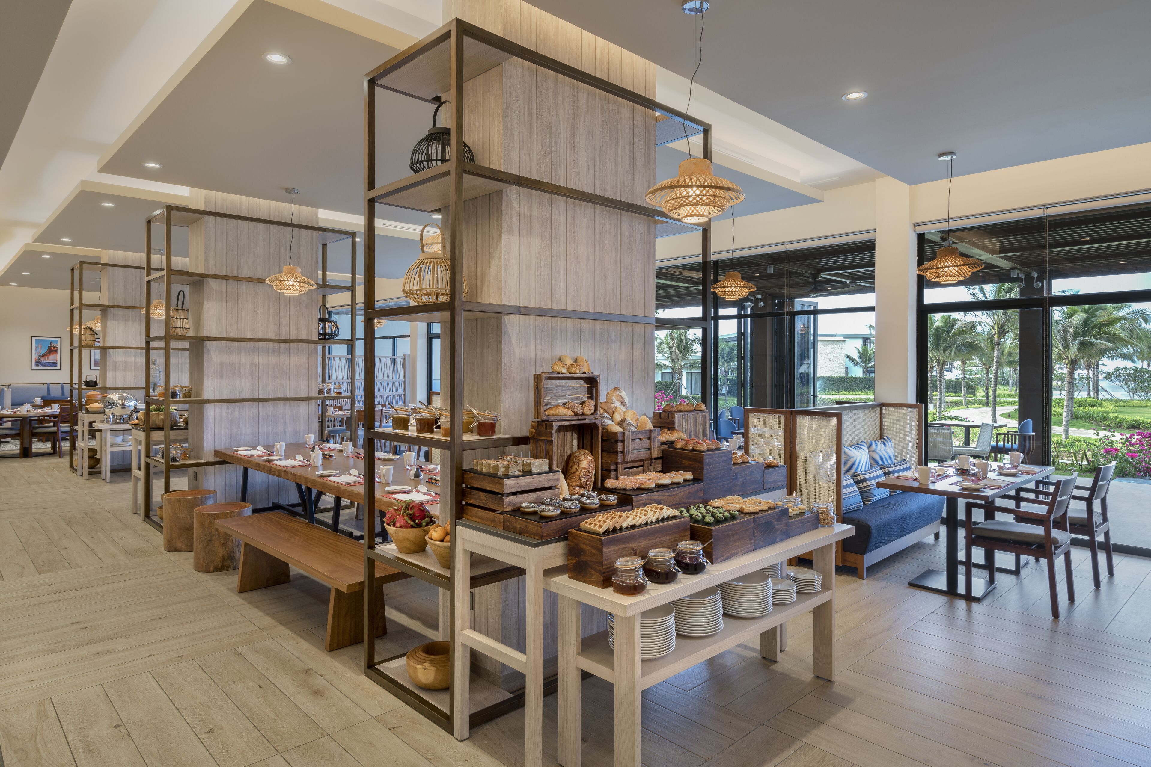 A spacious cafe with wooden furniture, a variety of baked goods, and hanging pendant lights.