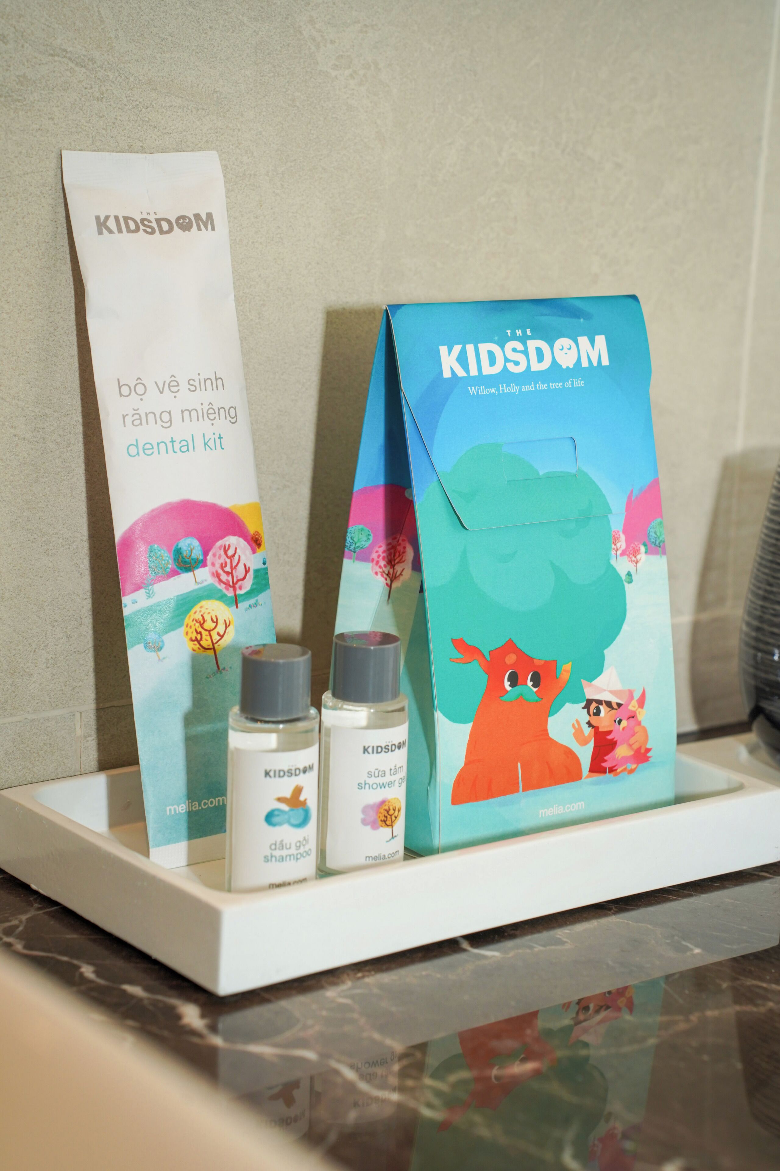 A bathroom shelf with a dental kit, shampoo, and a Kidsom book.