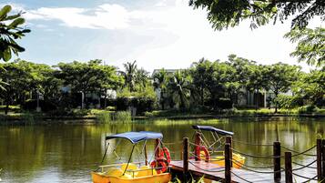 Un entorno tranquilo junto al lago, con dos botes amarillos anclados en un muelle de madera, rodeado de vegetación exuberante y un cielo despejado.