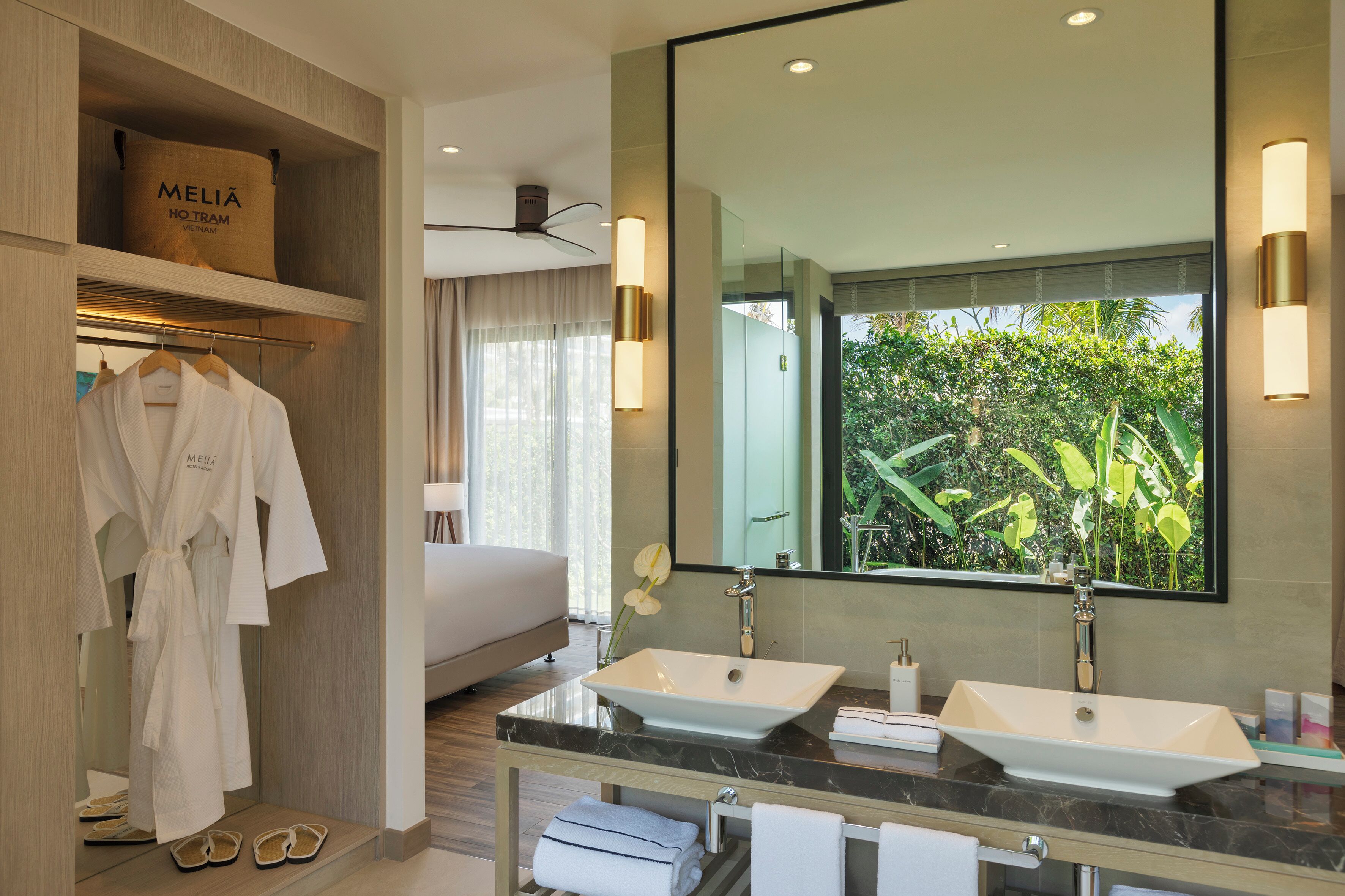 Un bagno d'hotel moderno con due lavandini, uno specchio grande e vista su piante verdi.