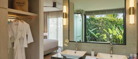 A modern hotel bathroom with two sinks, a large mirror, and a view of greenery outside.