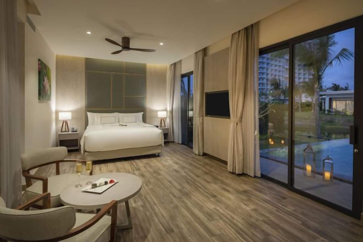 Een hotelkamer met een bed, een ronde tafel en uitzicht op een zwembad en palmbomen.