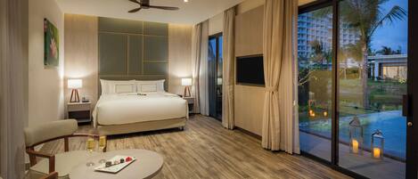 Habitación de hotel con cama, mesa de comedor, televisión y vista a una piscina y palmeras.
