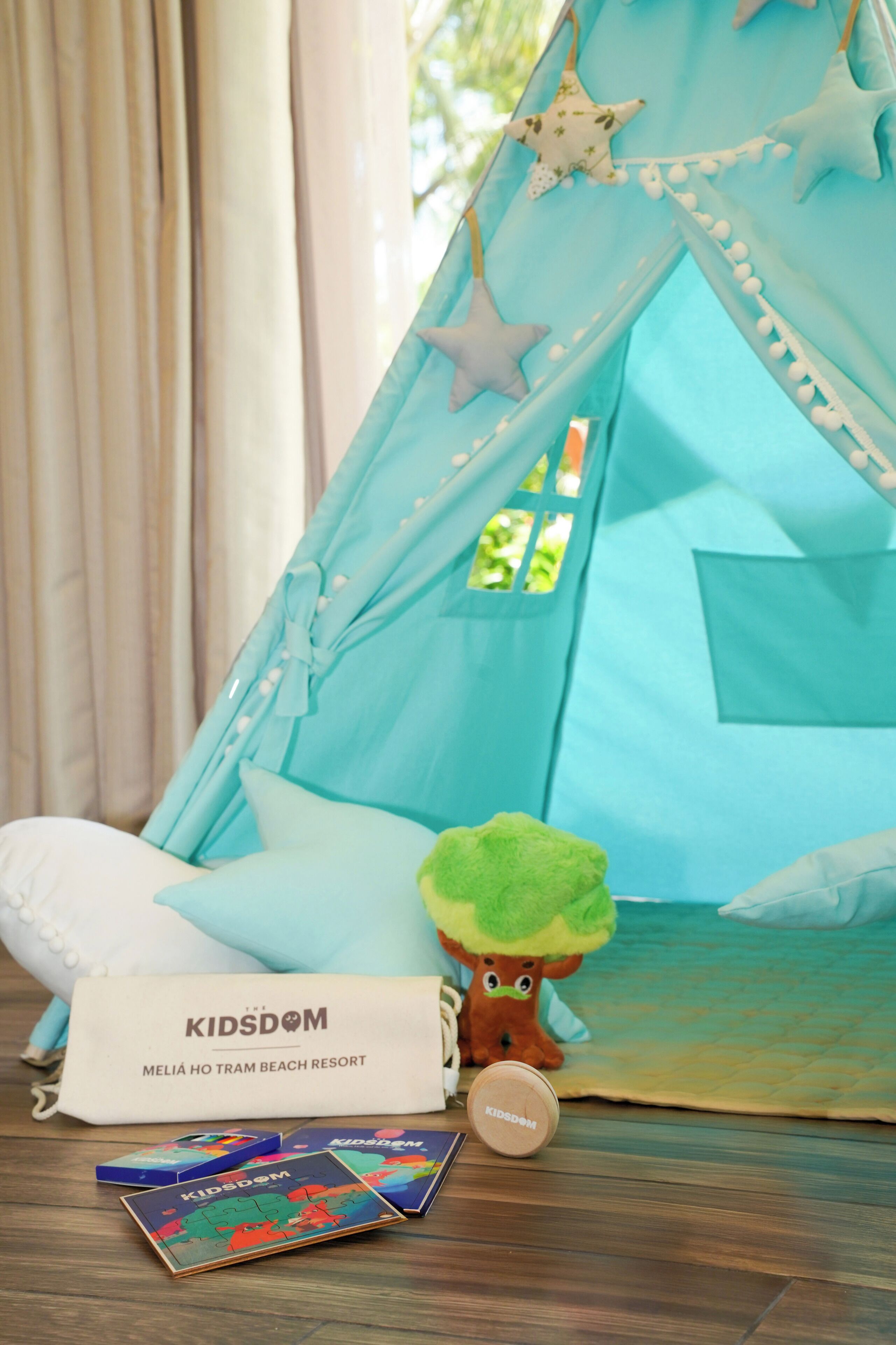 A tent with a star design, a plush toy, and a bag labeled "KIDSDOM" on a wooden floor.