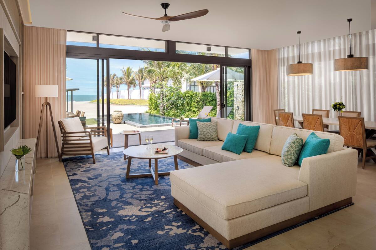 Een moderne woonkamer met een bank, salontafel en uitzicht op een zwembad en strand.
