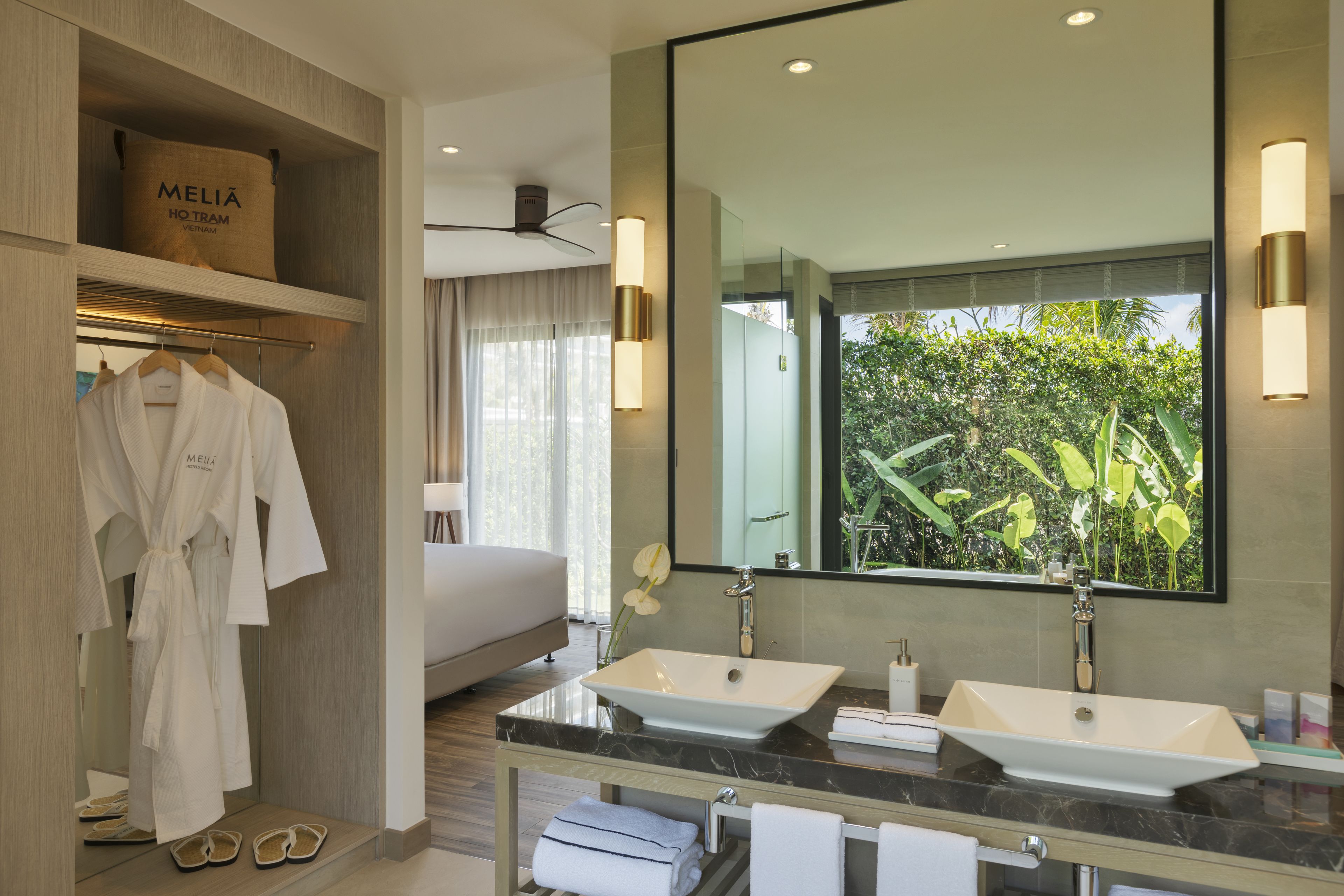 A modern bathroom with two sinks, a large mirror, and a robe rack with towels.