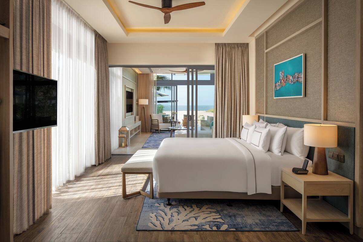 Een hotelkamer met een bed, nachtkastje, televisie en uitzicht op het strand.