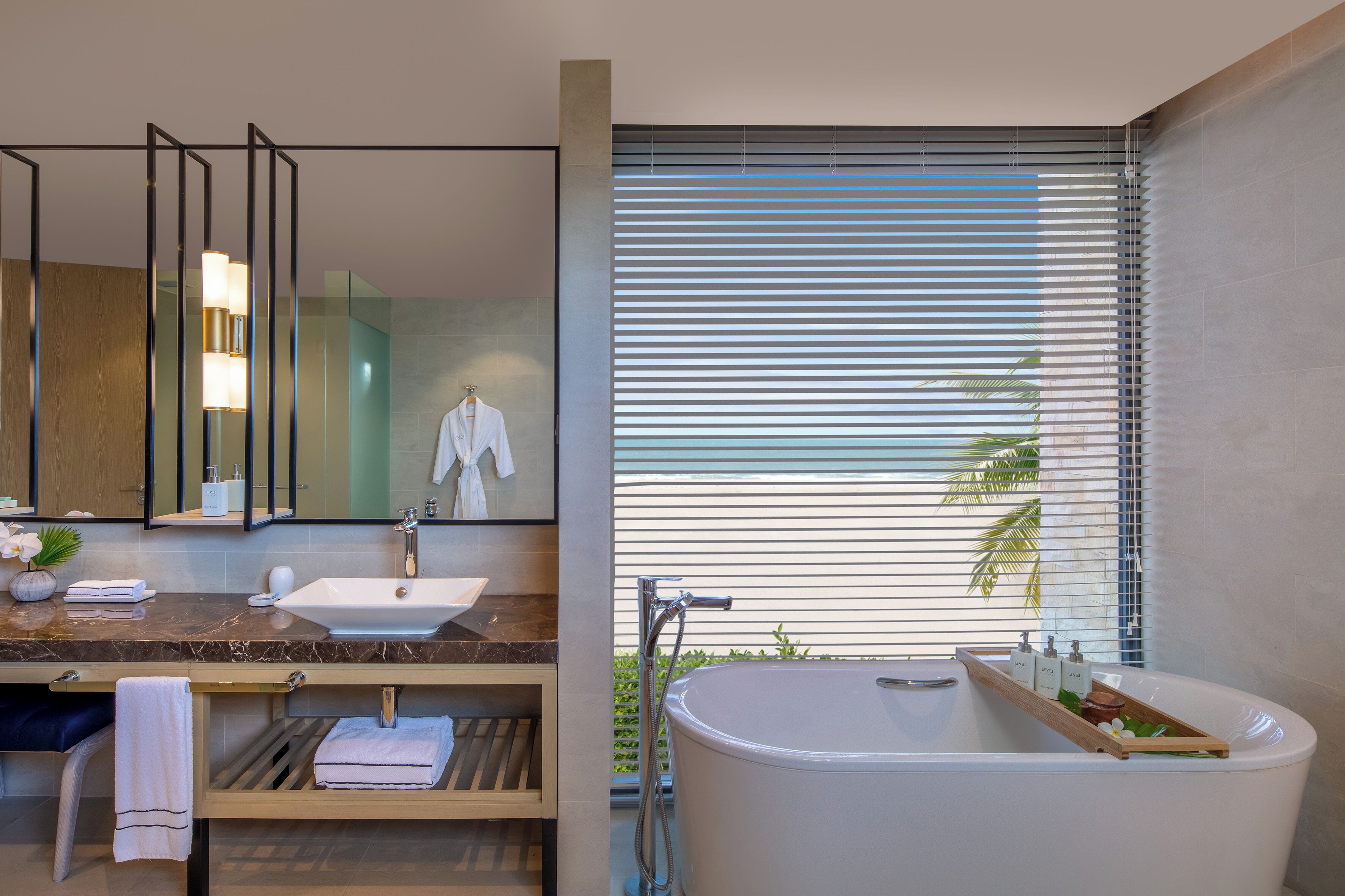 Un baño moderno con encimera de mármol, un lavabo blanco, una bañera y un amplio ventanal con persianas.