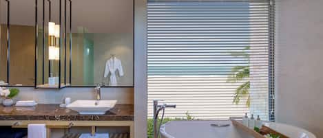 Un baño moderno con encimera de mármol, un lavabo blanco, una bañera y un amplio ventanal con persianas.