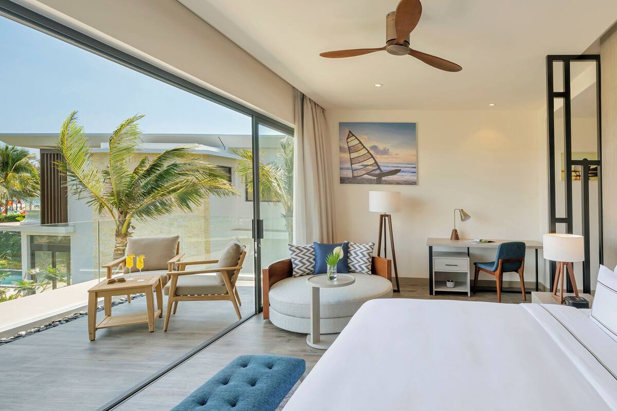 Een moderne hotelkamer met balkon, bed, bureau en stoel.