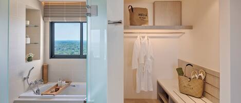 Ein modernes Badezimmer mit einer Badewanne, Ablagen für Toiletartikel, einem Fenster mit Blick, einem Handtuchhalter und einer Bank mit einer Tasche.