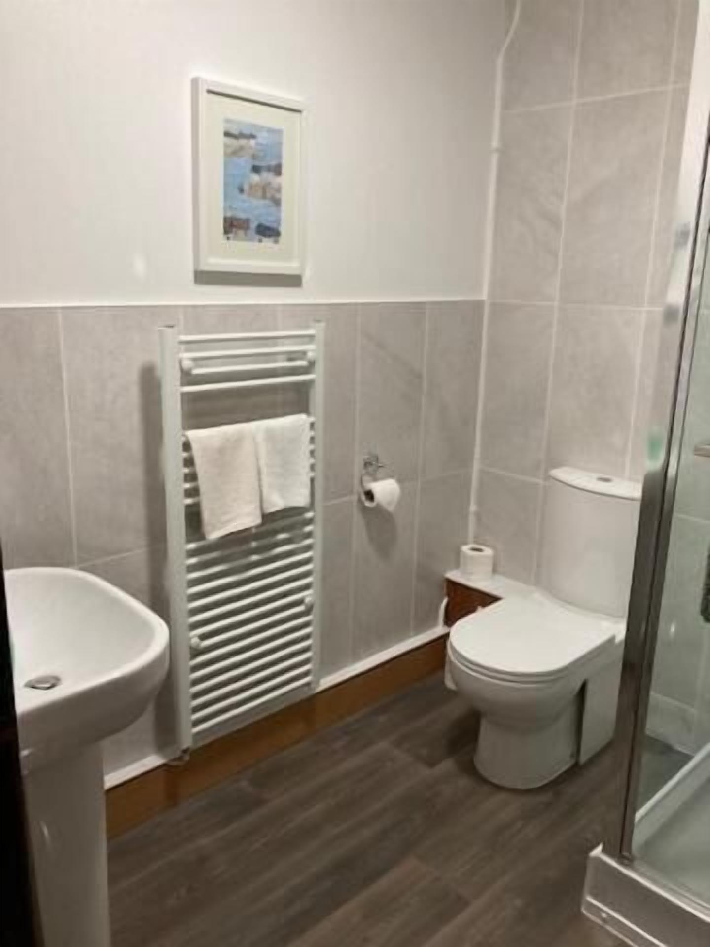 Un bagno con doccia, toilette e lavandino, caratterizzato da un pavimento piastrellato e un porta asciugamani.