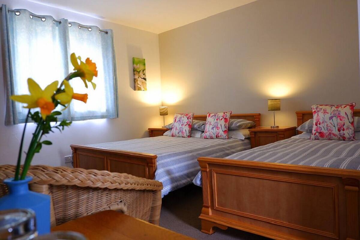 Una habitación de hotel con dos camas de madera, una silla de mimbre, una mesita y un jarrón con flores.