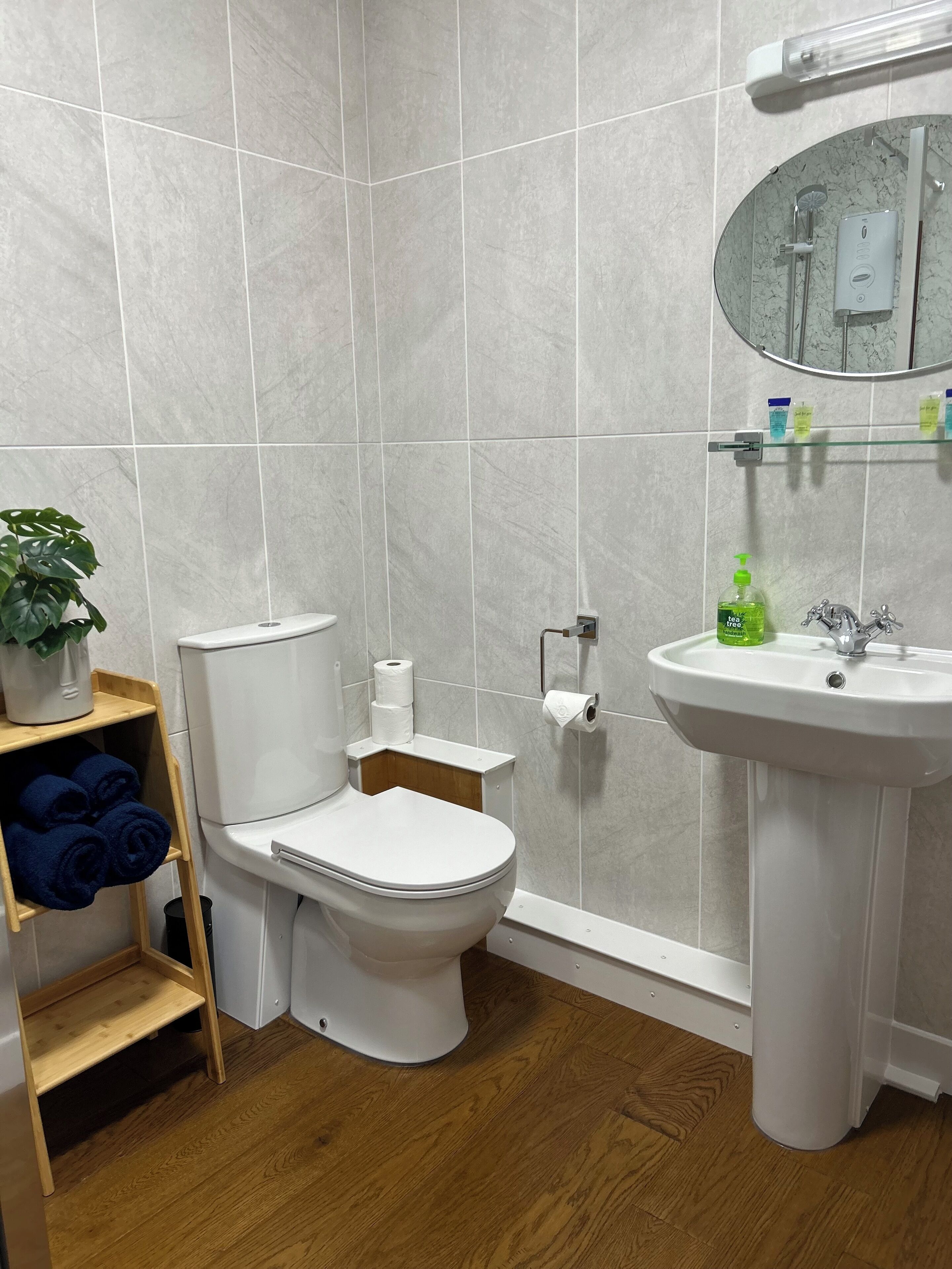A bathroom with a toilet, sink, mirror, and a shelf with towels.