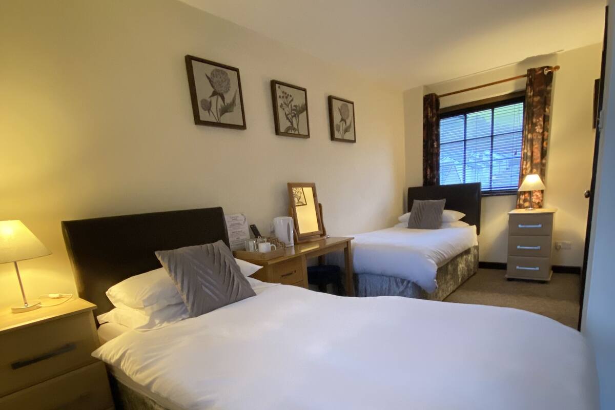 Habitación de hotel con dos camas, un escritorio, una silla, una lámpara y cuadros en la pared.