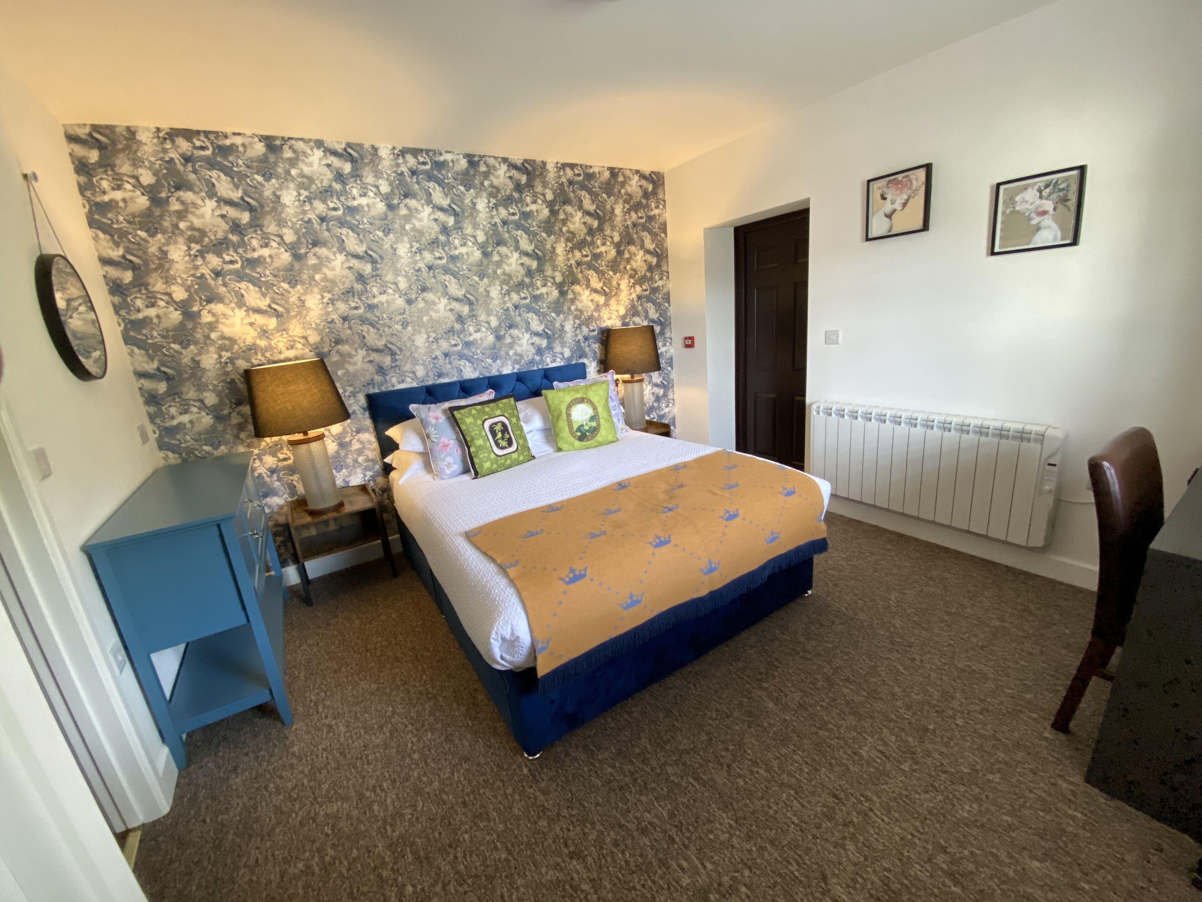 A bedroom with a large bed, two bedside lamps, a radiator, and a blue cabinet.