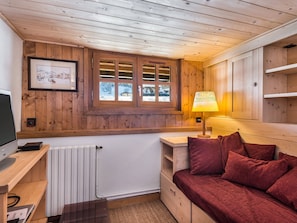 Ein gemütliches Blockhauszimmer mit Holzwänden, einem Fenster mit Blick auf eine verschneite Landschaft, einem Bett mit roter Bettwäsche, einer Lampe und einem Heizkörper.