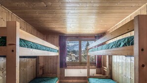 A cabin with two bunk beds, wooden walls, a large window with a mountain view, and a white radiator.