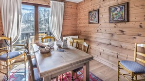 A wooden cabin with a dining area featuring a table and chairs, a window with curtains, and two framed pictures on the wall.