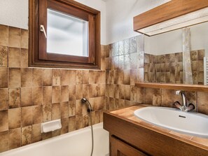 Un baño con bañera, lavamanos y ventana sobre el espejo.
