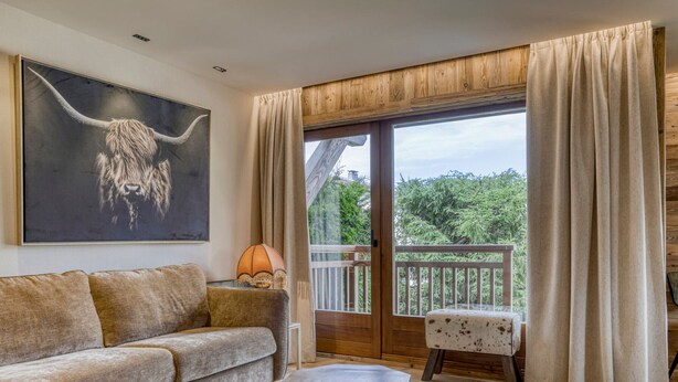 A cozy living room with a sofa, two wooden tables, a lamp, and a large painting of a bull's head. - Charming 1-bedroom near Megève slopes (Megève)