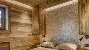 A bedroom with a wooden ceiling and walls, a bed with two pillows, a nightstand with a lamp, and a radiator. - Charming 1-bedroom near Megève slopes (Megève)