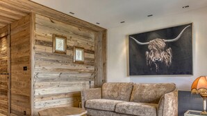 A modern living room with a wooden wall panel, a large sofa, two coffee tables, and a framed artwork of a bull's head. - Charming 1-bedroom near Megève slopes (Megève)