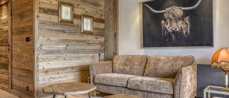 A modern living room with a wooden wall panel, a large sofa, two coffee tables, and a framed artwork of a bull's head.