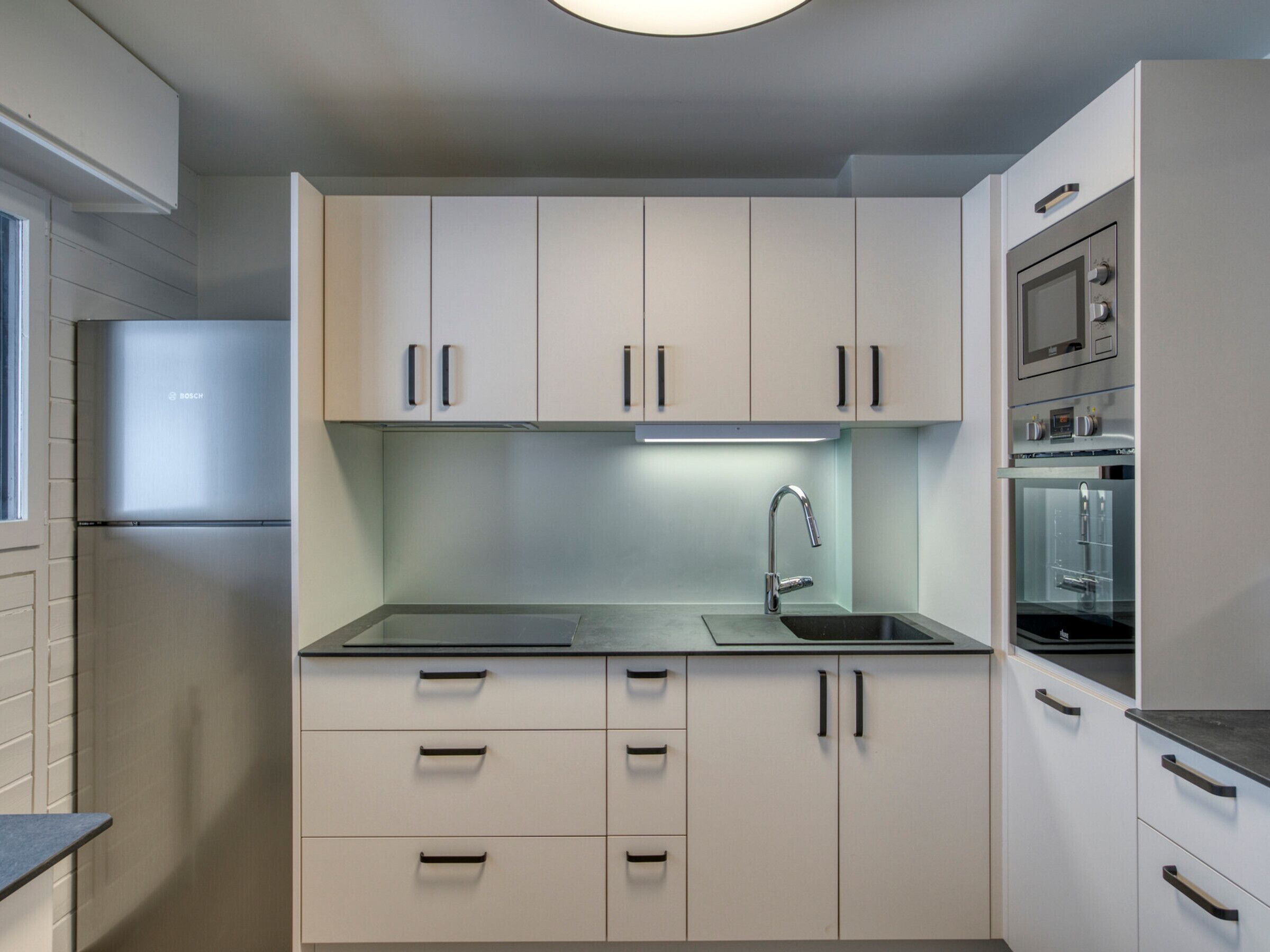 A modern kitchen with white cabinets, a stainless steel sink, and a Bosch refrigerator.