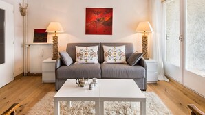 Ein gemütliches Wohnzimmer mit einem grauen Sofa, zwei passenden Lampen, einem weißen Couchtisch und einem roten abstrakten Gemälde an der Wand.