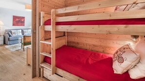 Ein Stockbett mit roter Matratze und einem Holz-Kopfteil in einem Raum mit Holzwänden und einem Sofa.