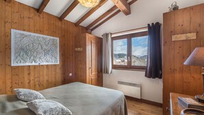 Une pièce chaleureuse aux murs en bois, un lit recouvert d’une couverture à motifs, une carte accrochée au mur, une fenêtre donnant sur l’extérieur et un radiateur.