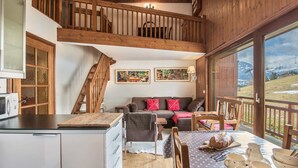 L’intérieur chaleureux d’un chalet avec un escalier en bois, un coin repas où la table est mise pour le petit-déjeuner, et un canapé agrémenté de coussins.