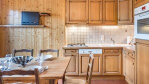 A kitchen with wooden cabinets, a gas stove, a dishwasher, and a television on a shelf.