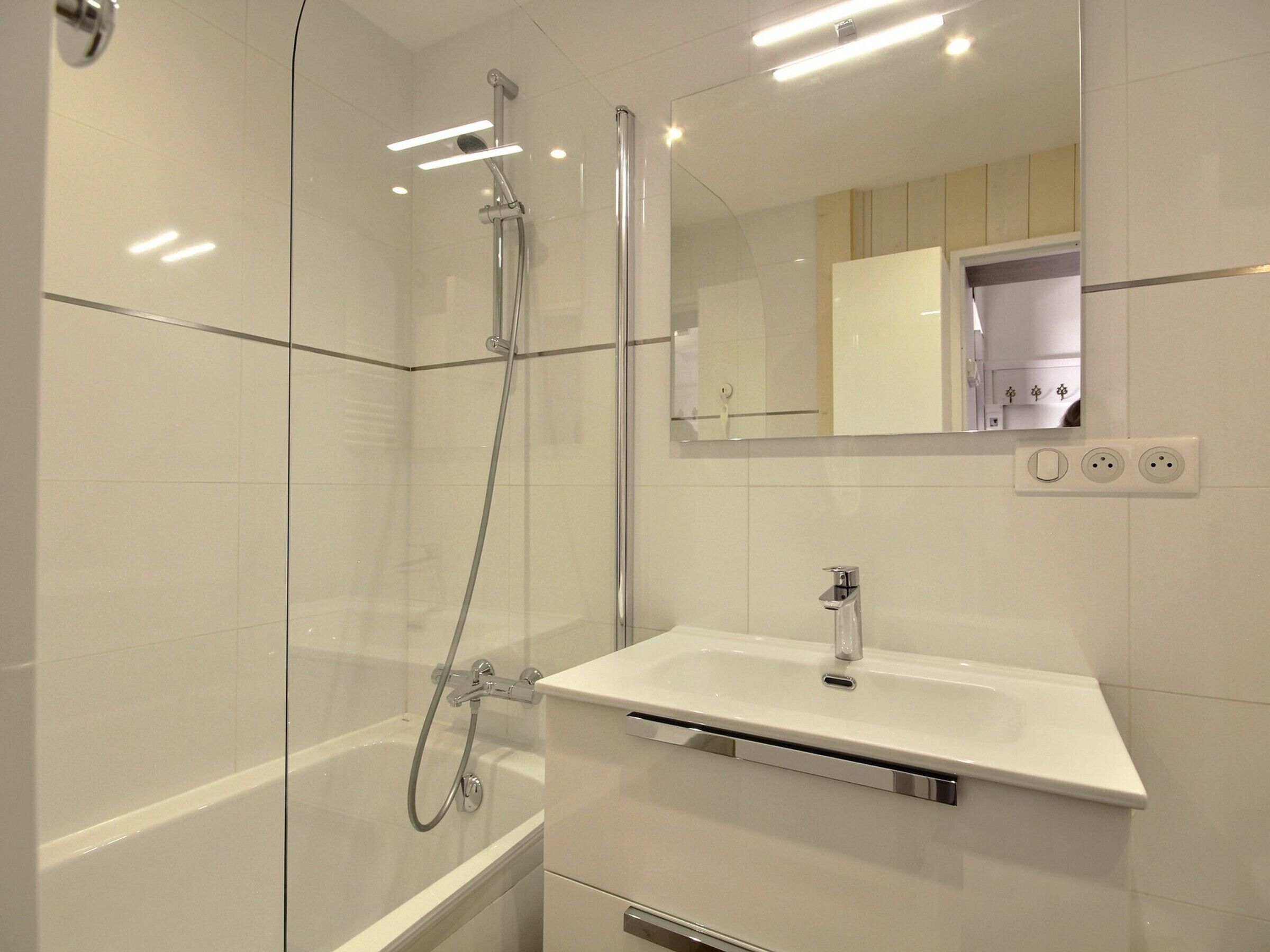Un baño moderno con ducha envuelta en vidrio, un lavamanos blanco y un espejo sobre él.