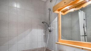 Een badkamer met een douche, wastafel en spiegel.