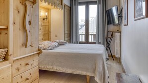 Een slaapkamer met een houten garderobe, een bed met een beddeken met een patroon, een televisie aan de muur en een raam met gordijnen.