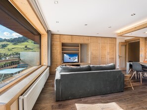 A modern living room with a large window, wooden panel walls, a grey sofa, and a television.